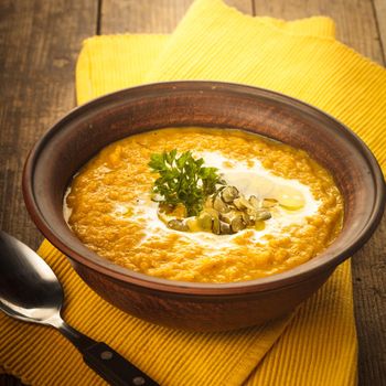 Pumpkin soup in clay bowl with spoon on the table