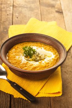 Pumpkin soup in clay bowl with spoon on the table