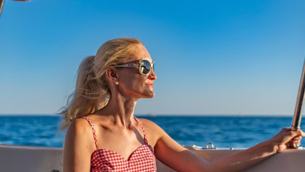 Beautiful lady sits on a boat, young with tender lips around the sea, the concept of well-being in summer sunglasses