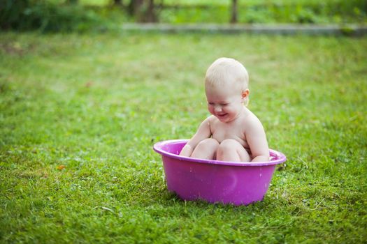 Happy toddler in a washbowl on the grass at the yard