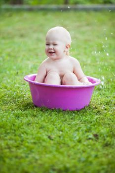 Happy toddler in a washbowl on the grass at the yard