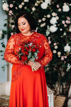 a woman in a red dress stands and holds a bouquet of red roses and strawberries in the interior