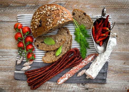 Wholemeal bread with dried salami sausages, tomatoes, greens, chili pepper on a wooden rustic table