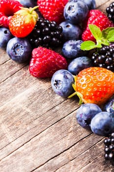 Summer wild berries over shabby wooden background. Raspberry, strawberry, blackberry and blueberry on the table