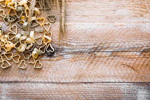 Heart shaped pasta with wheat ears on a wooden textured table