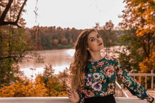 Cheerful stands leaning on a white railing of a young blonde in a colored shirt, having, an innocent autumn professional facial expression on a background of steps in a dark mask blue eyes