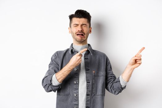Crying man whining and complaining, pointing fingers right at sad news, standing miserable on white background.