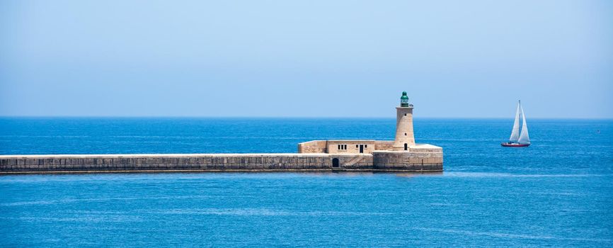 lighthouse in Valletta port of Malta on misty sea background with a ship