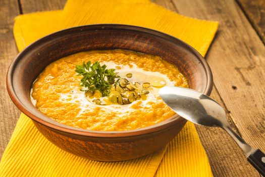 Pumpkin soup in clay bowl with spoon on the table