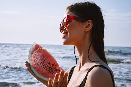 cheerful woman in black swimsuit eating watermelon on the beach. High quality photo