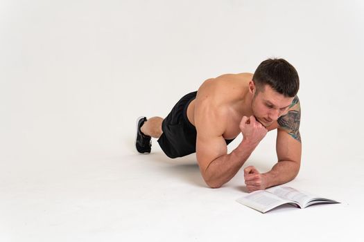 Bodybuilder reads the book on a white background isolated at the bottom of his head on his hands male young macho, athlete strong person guy shirtless, intellectual fit. Smile winner gym, strength tan