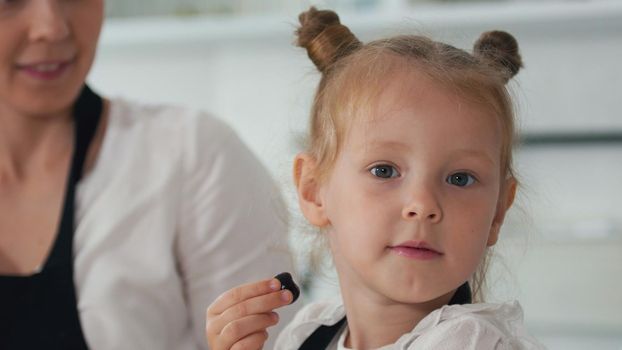 Portreat of a cheerful little girl licks a berry and looking at the camera, close up