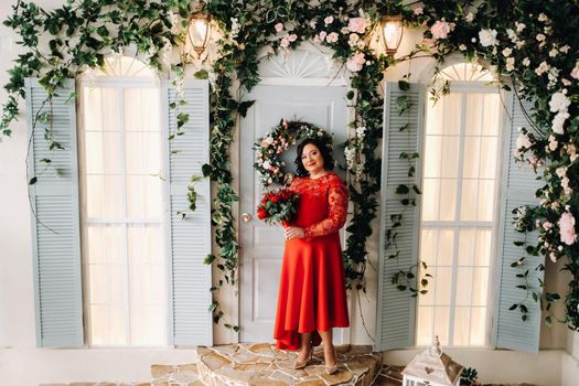 a woman in a red dress stands and holds a bouquet of red roses and strawberries in the interior