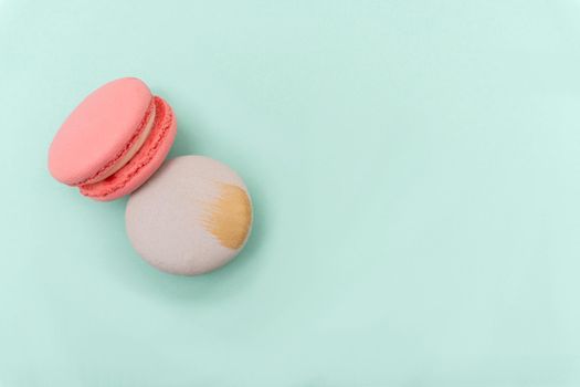 Two french cookies macaron or macaroon, pink strawberry and gray grapefruit lay on mint or turquoise background, view from the top, copy space, pastel colors