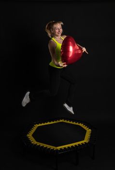 Girl on a fitness trampoline on a black background in a yellow t-shirt trampoline fit woman, equipment exercise training lifestyle movement, workout bounce. Wellness sportswear muscle instructor enjoy