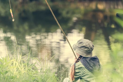 little fisher girl holds a rod sitting near a river
