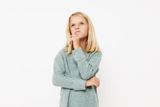 Beautiful little girl in a sweater, grimaces on a light background. High quality photo