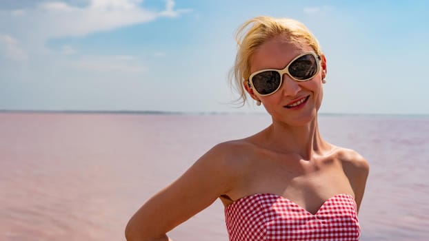 Cheerful woman in a beautiful dress young with beautiful eyes on the background of a red lake during the day and in summer