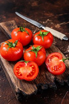 Cut Red cherry tomatoes on wooden cutting board. Dark background. Top view.