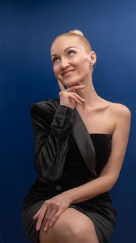 A tipsy young senior sits on a chair in a black suit with beautiful eyes on a purple background in bright daylight. Flaunts