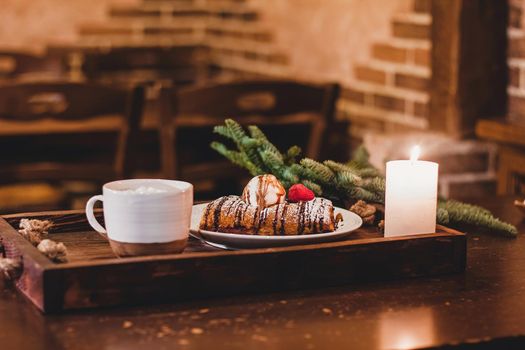 Closeup of a strudel with a strawberry on a Christmas plate near bamboo branch. Christmas breakfast on a wooden table