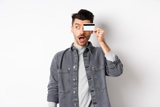 Excited funny guy look aside at logo and show plastic credit card, standing amazed on white background.
