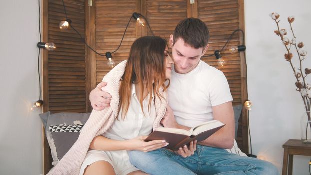 Young guy and girl sitting on the couch, laughing, flirting and having fun with a lights, love and family relations