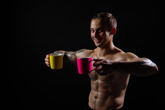 Man on black background keeps dumbbells pumped up in fitness bodybuilding arm training athletic heavy, male pectoral. handsome power, people fit holds a yellow and pink cup
