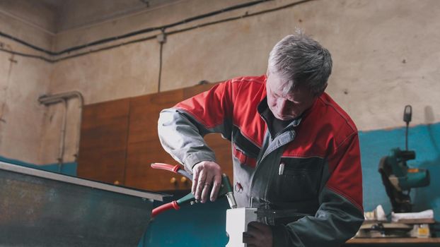 Worker assembling the metal part by hand with pliers, tools for grinding metal and metal details in the foreground, industrial concept