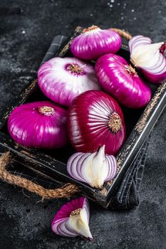 Flat red sweet onion in a wooden tray. Black background. Top View.