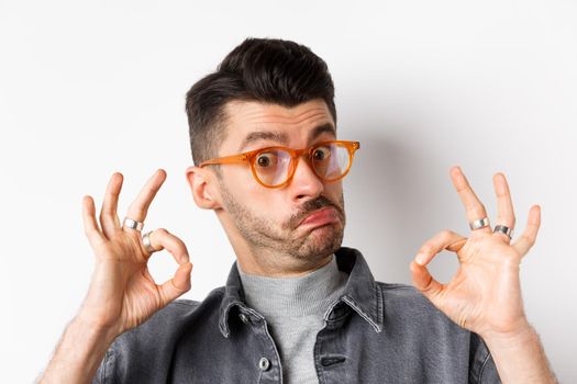 Not bad. Impressed man in stylish glasses showing okay signs and nod in approval, prase good thing, making compliment, standing on white background.