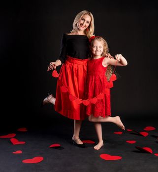Together, mother and daughter hold garlands of red Valentine's hearts, heart flirt, on the floor hearts romance wedding. art. emotions forever, hearts in a red dress girl, barefoot