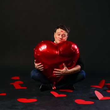 valentines red heart, an inflatable balloon in hands, handsome gay. On a black background hipster is fashionable,