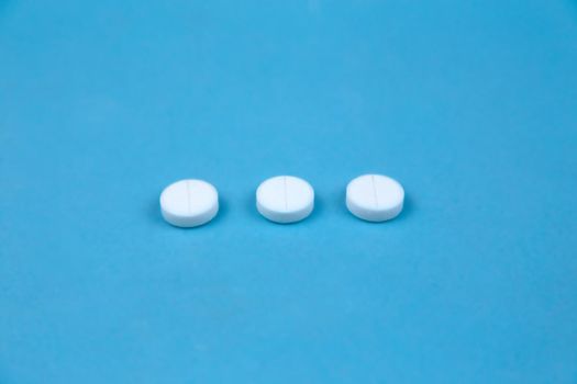 Three white round pills on blue background. Concept of healthcare and medicine communication
