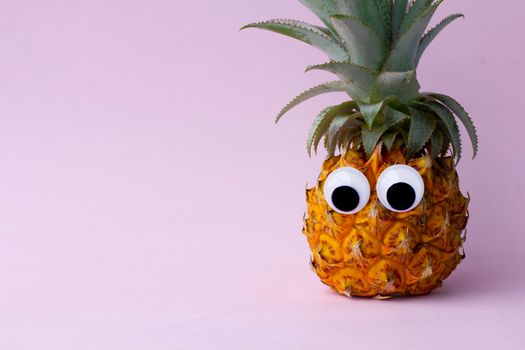 Funny exotic pineapple with googly eyes on pink background, closeup