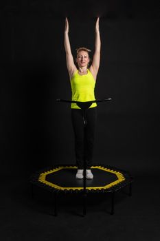 Girl on a fitness trampoline on a black background in a yellow t-shirt fit equipment activity female girl vitality, workout rebounder. mini trainer, young muscle instructor enjoy