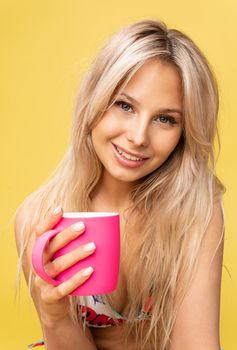 A girl sitting on the floor with her feet cross-legged keeps her head on a beautiful yellow background with a cup in hand yellow or pink and red girl, young beautiful studio white, people summer. Summertime adult sun soppy