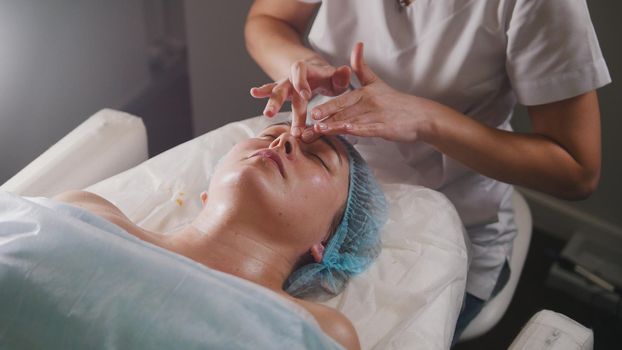 Woman doctor performes cosmetic procedure - mask facial massage at spa salon skincare, close up