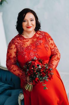 a woman in a red dress sits on a sofa and holds a bouquet of red roses and strawberries in the interior