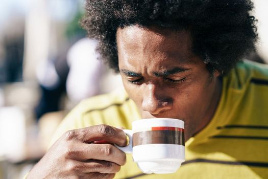 Cuban Black Man enjoying coffee in cafe while sitting at the table outdoors on his trip to Granada, Spain.