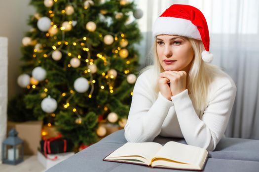 Beautiful young woman praying in front of the decorated Christmas tree