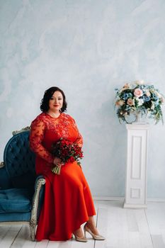 a woman in a red dress sits on a sofa and holds a bouquet of red roses and strawberries in the interior