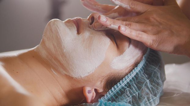 Female doctor performes cosmetic procedure - mask facial massage at spa salon skincare, close up