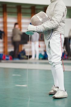 Participant of the fencing tournament with rapier and protective mask in hands, telephoto shot