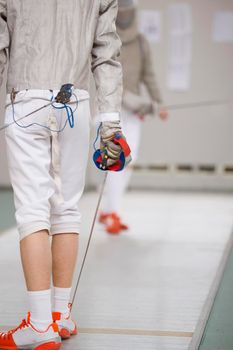 Rear view shot of teenage fencer in white clothes on the fencing tournament, close up