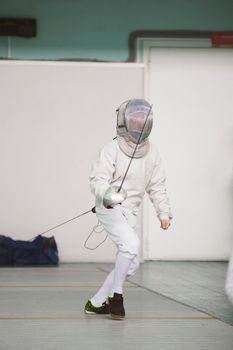 Boy teenager fencer in special costume at the fencing competition with rapier ready for fight, telephoto shot
