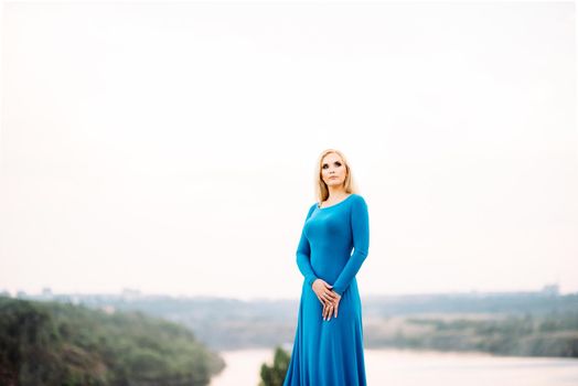 blonde girl in a blue dress with blue eyes in a granite quarry against the background of gravel