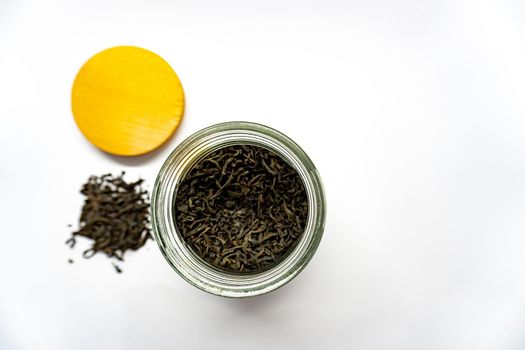 Black tea in glass jar, pounch of the tea and yellow bamboo cover are on white background, view from the top