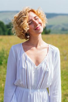 Beautiful blonde woman with short curly hair outdoors. Romantic model in summer white dress.
