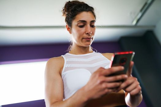 Athletic woman consulting her training on her smart phone at the gym